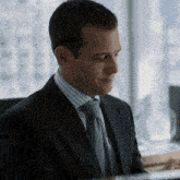 a man in a suit and tie sits at a desk in front of a window