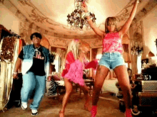 a man and two women are dancing in a room with a chandelier