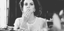 a woman is covering her mouth with her hand while smoking a cigarette .