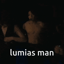 a shirtless man is being held by a woman in a dark room with the words lumias man written on the bottom .