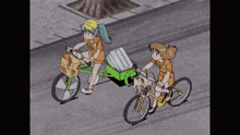 two girls are riding bicycles down a street with a green trailer attached to them .