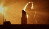 a silhouette of a woman standing in front of a burning building