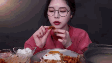 a woman wearing glasses is eating a plate of food with a fried egg on top .