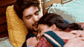 a man and woman are laying on a bed and the woman is kissing the man 's forehead .