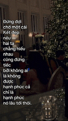 a woman sits at a table in front of a christmas tree with foreign writing on it