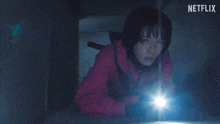 a woman in a red jacket is holding a flashlight in the dark .