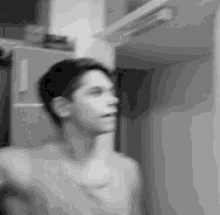 a black and white photo of a shirtless man in a kitchen .