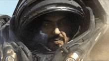 a man in a space suit looks at the camera with his hand on his chin