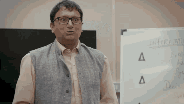 a man wearing glasses stands in front of a white board that says information