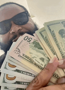 a man wearing sunglasses holds a stack of 50 dollar bills in front of his face