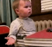 a baby is sitting at a table wearing a bib and making a face .