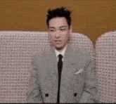 a man in a suit and tie is sitting on a couch with his hands out .