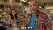 a man in a plaid shirt says wait for it in front of a woman in a store