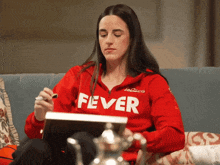 a woman sitting on a couch wearing a red sweatshirt that says fever