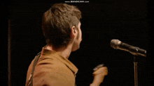a man in a brown shirt is playing a guitar in a dark room