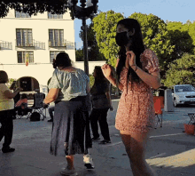a woman wearing a mask stands on a sidewalk with other people