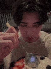 a man is eating strawberries and blueberries with a spoon .
