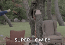 a man is wearing a cape and standing in front of a chair in a park .