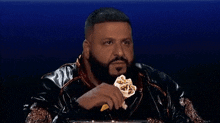 a man with a beard is sitting in a chair eating a piece of food .