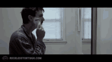 a man is shaving his face in front of a window and the website recklesstortiga.com is displayed