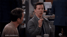 two men sit at a table with a cup that says just the tip