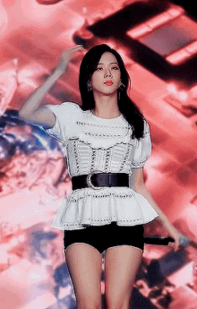 a woman in a white top and black shorts is holding a microphone on stage .