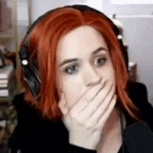 a woman with red hair is covering her mouth with her hand while wearing headphones .