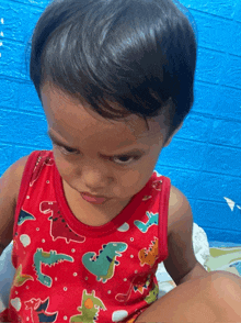 a little boy in a red tank top with dinosaurs on it
