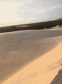 a person is walking on a sand dune with a body of water in the background