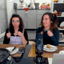 two women are sitting at a table with plates of food and a microphone