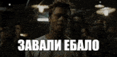 a man in a white shirt stands in a dark room with the words " завали ебалo " above him