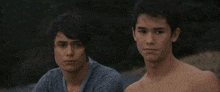 two young men without shirts are sitting next to each other looking at the camera .