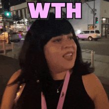 a woman in a black tank top with a pink lanyard around her neck says " wth "