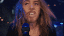 a man with long hair and a beard is singing into a microphone with the words " did you r " behind him