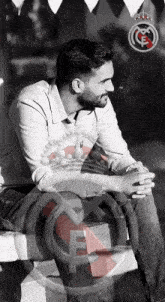 a black and white photo of a man sitting on a bench with a real madrid logo behind him