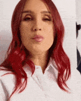 a woman with red hair is wearing a white shirt and making a kiss .