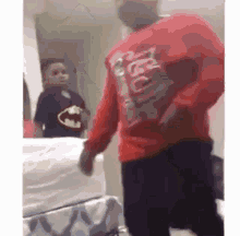 a man in a batman shirt is standing in front of a bed