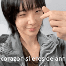a woman in a gray jacket is pointing at her face with the words corazon si eres de ann written on the bottom