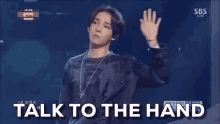 a man is standing on a stage with his hand up and the words `` talk to the hand '' written on the screen behind him .