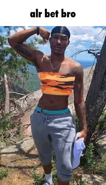 a man wearing a crop top is standing next to a tree on top of a mountain .