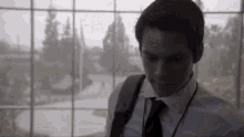 a man in a suit and tie is standing in front of a window looking down .