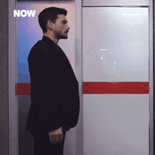 a man in a suit is standing in front of a door with the word now on it