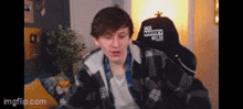 a young man in a plaid jacket is sitting in a chair with a black hat that says masters plus .