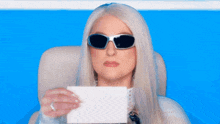 a woman wearing sunglasses holds a piece of paper