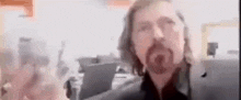 a man with long hair and a beard is standing in front of a computer monitor .