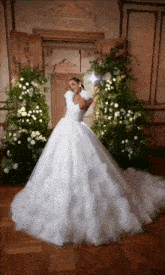 a woman in a wedding dress is standing in front of a floral arrangement