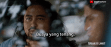 a man with a beard is looking out a window with the words buaya yang tenang