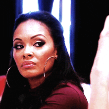 a woman wearing hoop earrings is looking at the camera with a serious look on her face