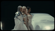 three women in white dresses are standing next to each other on a white surface