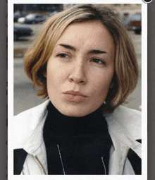 a close up of a woman 's face with a black turtleneck and a white jacket